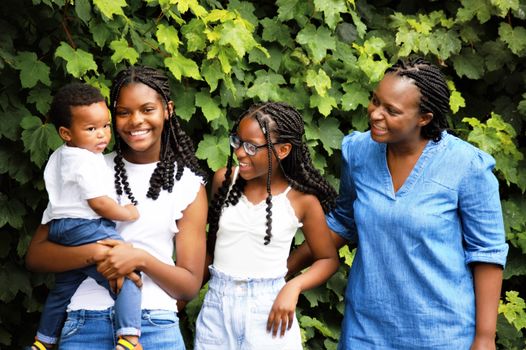 A joyful family photo featuring black women and children with braided hair, enjoying an outdoor photoshoot.