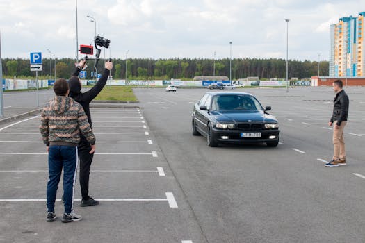A film crew with a camera rig directs a car scene in an outdoor parking lot.