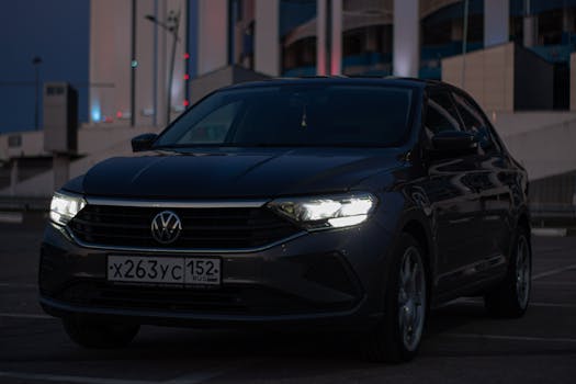 A Volkswagen car with headlights on, parked outdoors at night, showcasing a dark and moody atmosphere.