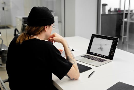 A focused designer in a beanie works on a laptop in a modern office.