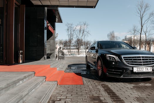 A luxury black sedan parked on a red carpet driveway outside a modern building.