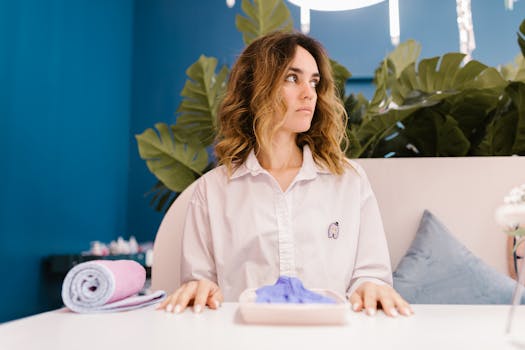A fashionable woman with dyed hair and a dress shirt sits in a salon, surrounded by stylish decor.