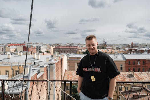 A young man stands on a rooftop overlooking St. Petersburg under a cloudy sky.
