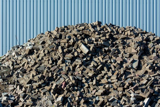 A large pile of rubble consisting of bricks and debris against a corrugated metal fence.