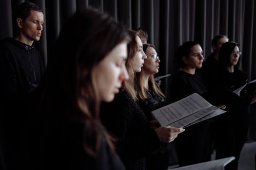 Adult choir practicing in an indoor studio performance setting with music sheets.