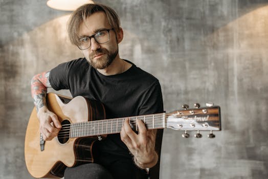 Tattooed man playing acoustic guitar indoors with focus on musical expression.