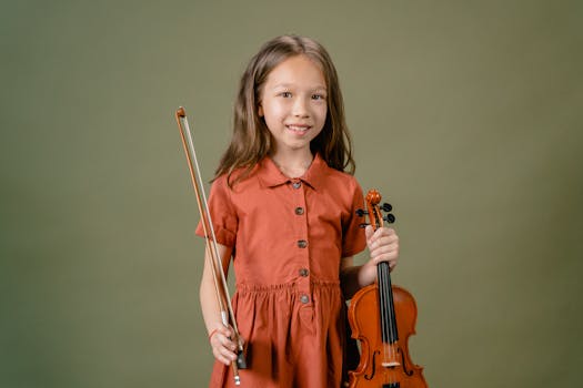 A young girl smiling while holding a violin and bow in a studio setting.