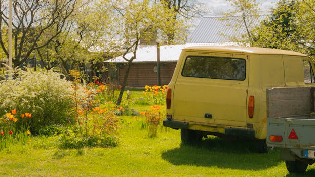A charming vintage yellow van parked in a blooming spring garden with vibrant flowers.