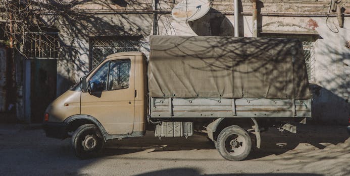 A vintage delivery truck parked on a sunlit urban street with textured walls in the background.