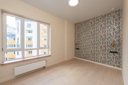 Interior of spacious empty room with laminate floor and colorful wall illuminated by ceiling lamp in new apartment