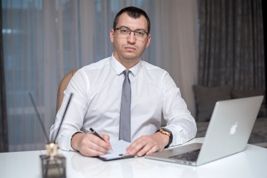 Professional man in corporate attire sitting at desk with laptop, engaged in work.