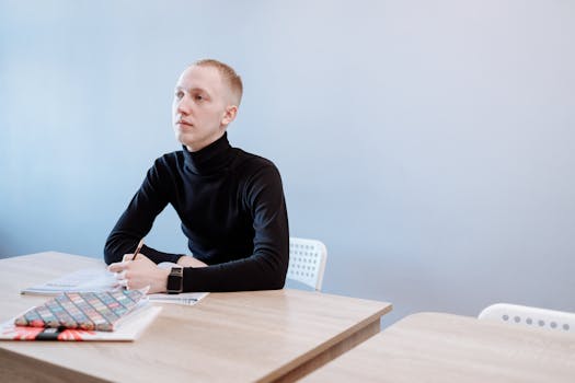 Young man in a black turtleneck writing at a desk, contemplating ideas.