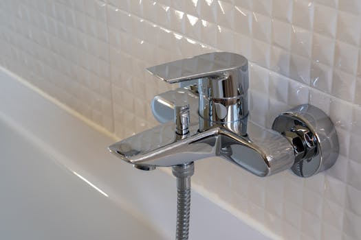 Close-up of a contemporary chrome faucet in a modern bathroom with white geometric tiles.