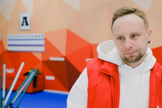 Serious male curling player in sportswear looking away with pensive face while standing near brooms and score board during game