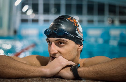 Close-up of a focused male swimmer in goggles and cap resting at the poolside indoors.