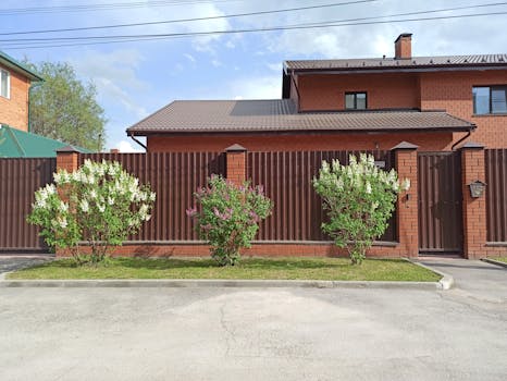 Elegant brick house with brown metal fence and flowering bushes in Berdsk, Russia