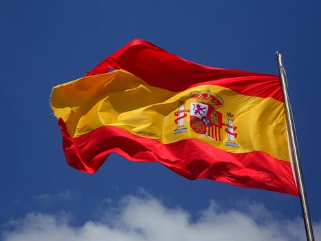 Vibrant Spanish flag waving against a clear blue sky and clouds.